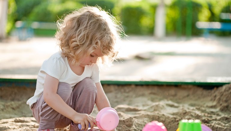 Child exploring outdoor sand play under natural sunlight
